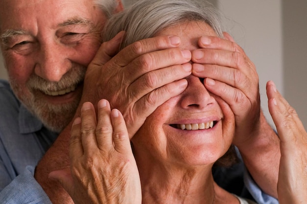 Starszy mężczyzna robi niespodziankę żonie dojrzała kobieta z tyłu zamyka oczy szczęśliwi i radosni starsi ludzie styl życia dom cieszy się wewnętrzną aktywnością rekreacyjną i rocznicą małżeństwa razem