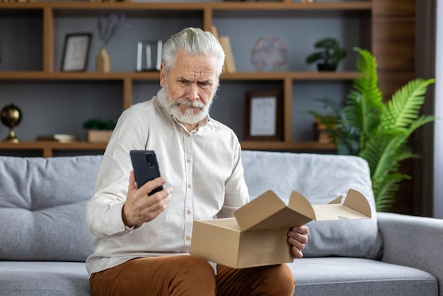 Zdjęcie starszy mężczyzna siedzący w domu na kanapie i trzymający zakup online w pudełku porównuje produkt z