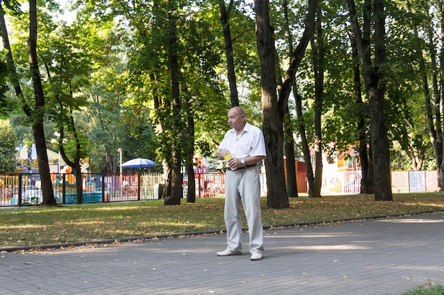 Starszy mężczyzna spaceruje samotnie po parku latem Emeryt w białej koszuli stoi samotnie w parku ze szklanką popcornu