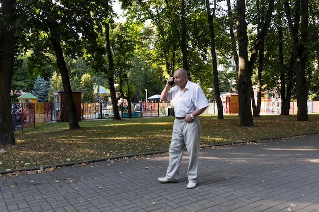 Starszy mężczyzna spaceruje samotnie po parku latem, nowoczesny emerytowany biznesmen w białej koszuli