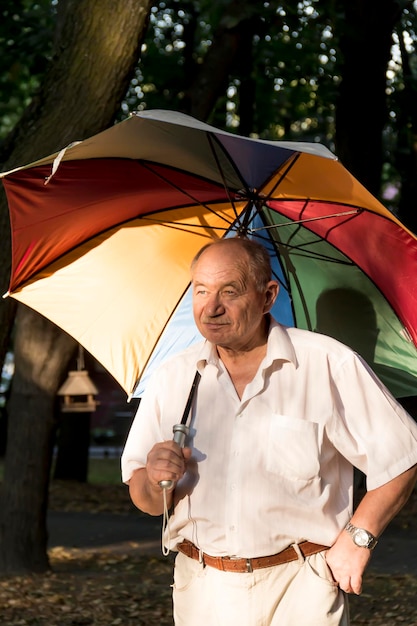 Starszy mężczyzna stoi pod dużym kolorowym parasolem Emeryt na spacerze po parku