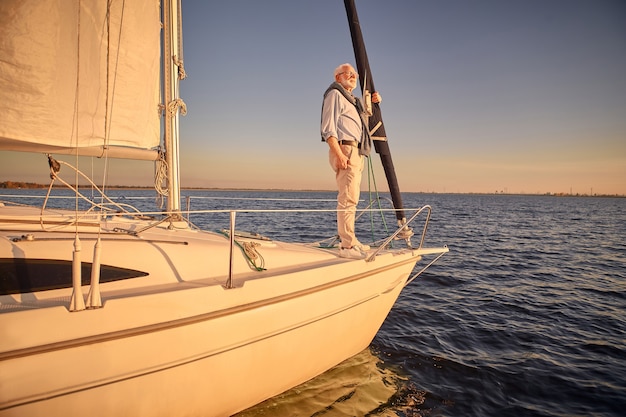 Starszy mężczyzna stojący z boku żaglówki lub pokładu jachtu unoszącego się w morzu, patrząc na horyzont