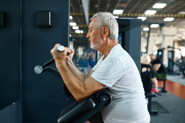 Zdjęcie starszy mężczyzna, trening na maszynie do ćwiczeń, wnętrze siłowni na tle. sportowy dziadek na treningu fitness w centrum sportowym. zdrowy styl życia, opieka zdrowotna, stary sportowiec