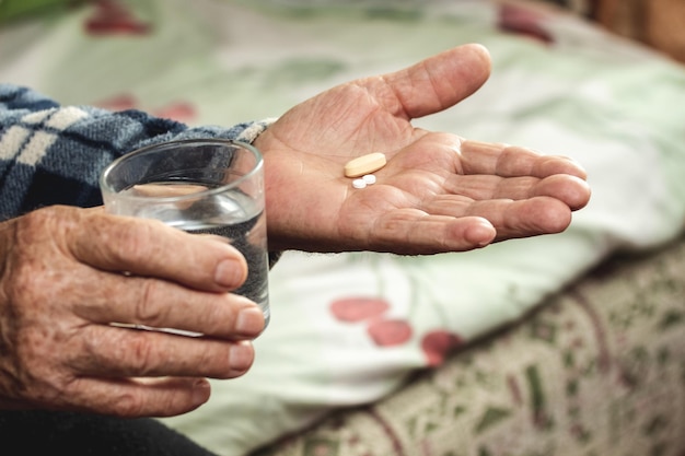Starszy mężczyzna trzyma w rękach pigułki i szklankę wody Zażywanie tabletek w leczeniu choroby