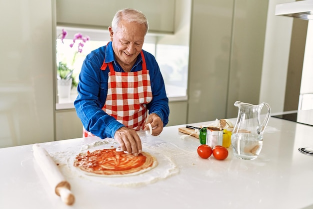 Starszy mężczyzna uśmiecha się pewnie gotowania pizzy w kuchni