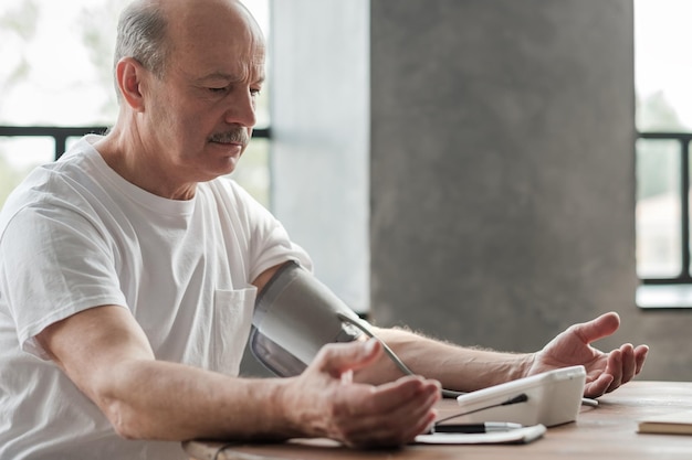 Starszy mężczyzna używający domowego urządzenia do pomiaru ciśnienia krwi, aby sprawdzić swoje parametry życiowe