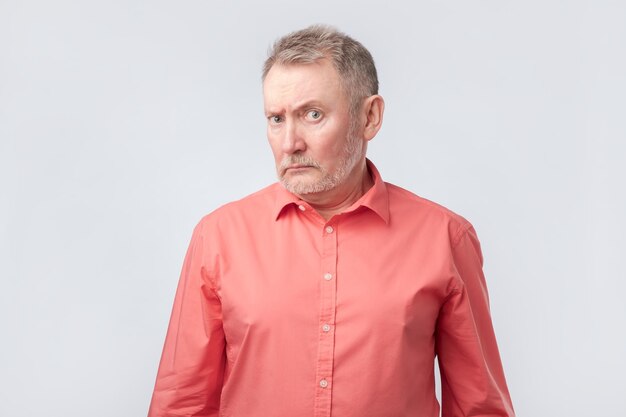 Starszy mężczyzna w czerwonej koszuli marszczy brwi i mruży oczy pokazując niedowierzanie lub wątpliwości