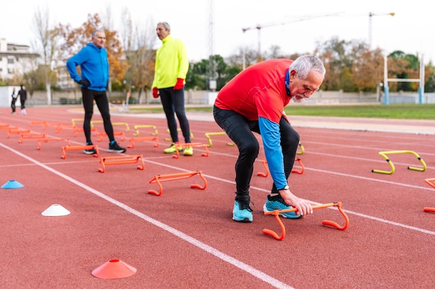 Starszy mężczyzna w czerwonym pochyla się, aby dostosować stożek treningowy z dwoma innymi omawiającymi sesję ćwiczeń