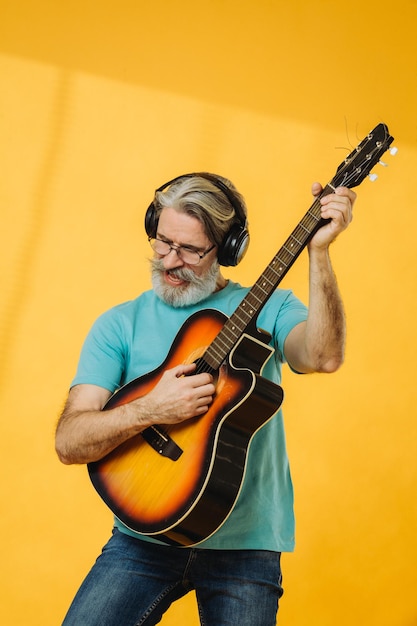 Starszy mężczyzna w okularach i słuchawkach gra na gitarze na żółtym tle Strzelanie w studio