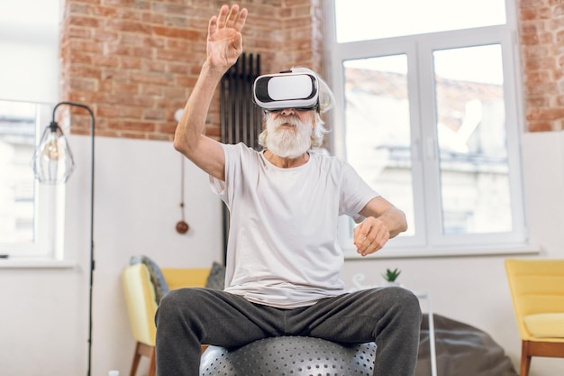 Starszy mężczyzna w okularach VR trenujący na fitball w domu