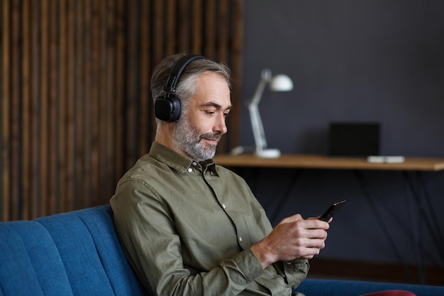 Starszy mężczyzna w słuchawkach słucha muzyki na smartfonie za pomocą aplikacji muzycznej portret przystojnego greyhai