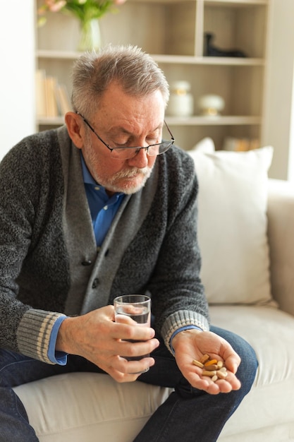 Starszy mężczyzna w średnim wieku trzymający pigułkę medyczną i szklankę wody. Dojrzały, starszy dziadek bierze