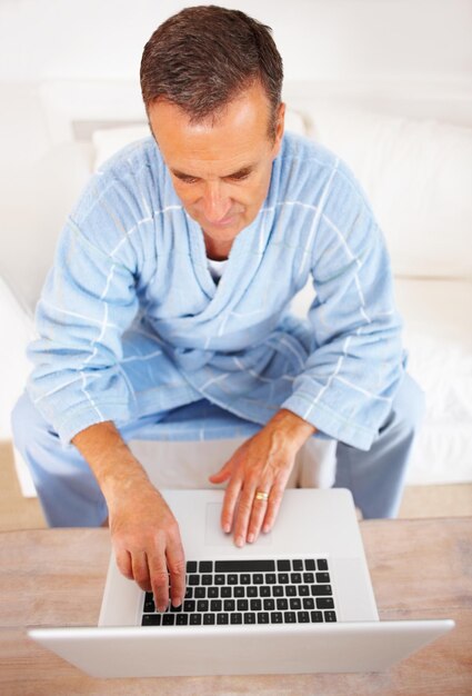 Starszy mężczyzna w szlafroku pracujący na laptopie w domu Widok od góry starszego emeryta pracującego na laptopie w domu