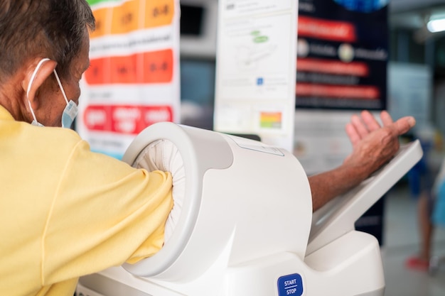 Starszy mężczyzna z Azji używający automatycznej maszyny do pomiaru ciśnienia krwi w szpitalu