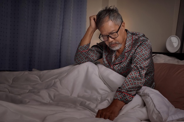 Starszy mężczyzna z przygnębioną i zestresowaną siwą brodą siedział w łóżku z powodu bezsenności