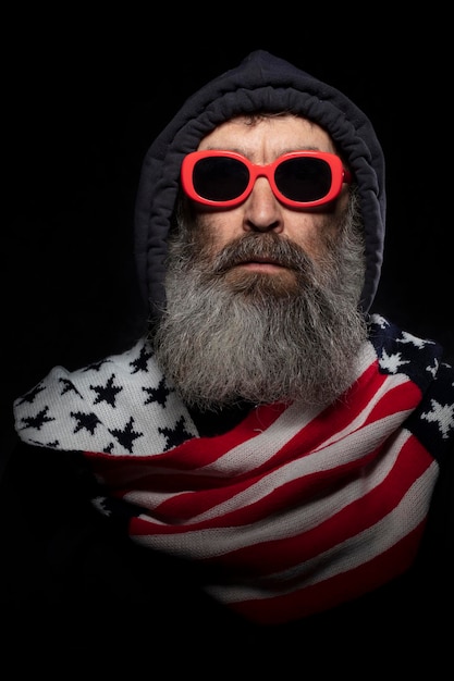 Starszy mężczyzna z siwą brodą w kapturze i szaliku z wzorem amerykańskiej flagi