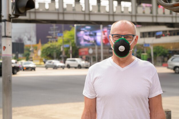 Starszy mężczyzna za pomocą maski do ochrony przed smogiem zanieczyszczeń w mieście