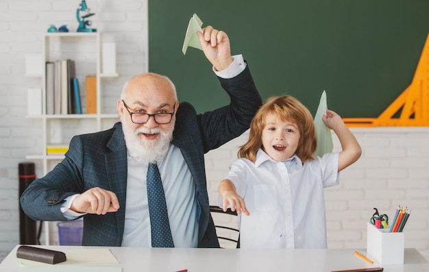 Starszy nauczyciel lub dziadek i uczeń trzyma papierowy samolot w klasie w szkole privat