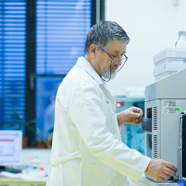 Starszy naukowiec płci męskiej prowadzący badania naukowe w laboratorium przy użyciu chromatografu gazowego o płytkiej kolorystyce DOF
