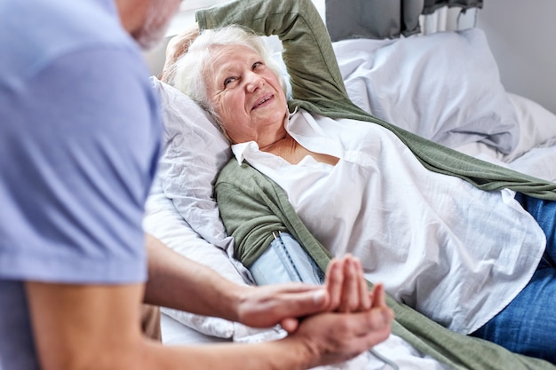 Starszy pacjentka w szpitalu z zaniepokojonym mężem trzymając się za ręce podczas sprawdzania ciśnienia krwi z tonometrem. człowiek pomaga, wspiera