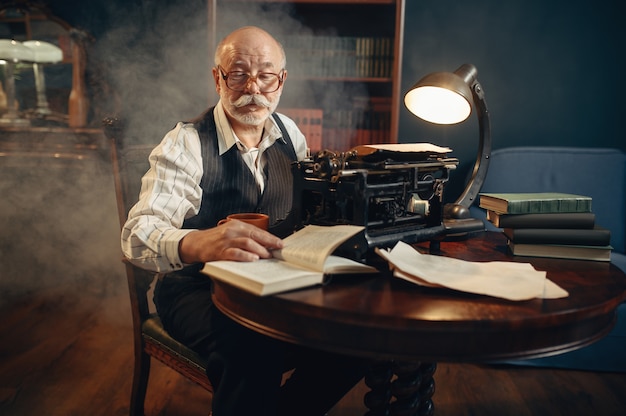 Starszy pisarz pracuje na starej maszynie do pisania w swoim domowym biurze. Stary człowiek w okularach pisze powieść literacką