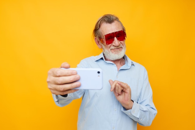Starszy siwy mężczyzna w modnych czerwonych okularach z telefonem na białym tle