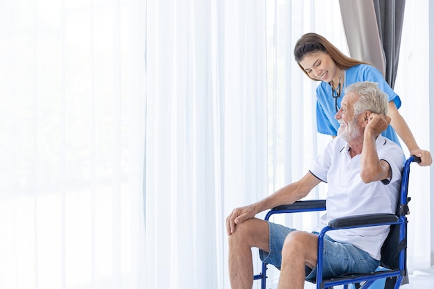 Starszy starszy mężczyzna siedzący na wózku inwalidzkim z szczęśliwym uśmiechem pielęgniarki w szpitalu opieki domowej