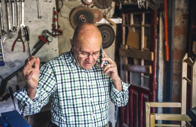 Zdjęcie starszy stolarz rozmawia przez telefon w swoim warsztacie