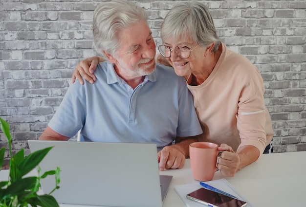 Starszy szczęśliwa para obejmująca przy użyciu laptopa razem uśmiechnięta rodzina czytająca wiadomości w podeszłym wieku