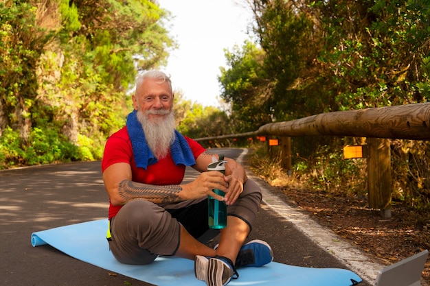 Starszy szczęśliwy uśmiechnięty mężczyzna z białą brodą odpoczywa podczas wykonywania ćwiczeń na świeżym powietrzu na przyrodę