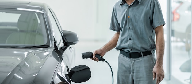 Starszy technik azjatycki ładuje samochód elektryczny lub EV w centrum serwisowym w celu utrzymania, ekologicznej koncepcji energii alternatywnej