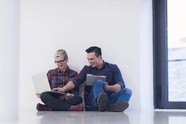 startupowy biznes i nowa koncepcja technologii mobilnej z młodą parą w nowoczesnym jasnym wnętrzu biurowym pracującym na laptopie i tablecie nad nowym kreatywnym projektem i burzą mózgów