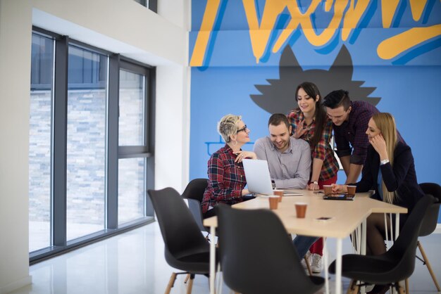 Startupowy zespół biznesowy na spotkaniu w nowoczesnym, jasnym wnętrzu biurowym, burza mózgów, pracujący na laptopie i tablecie