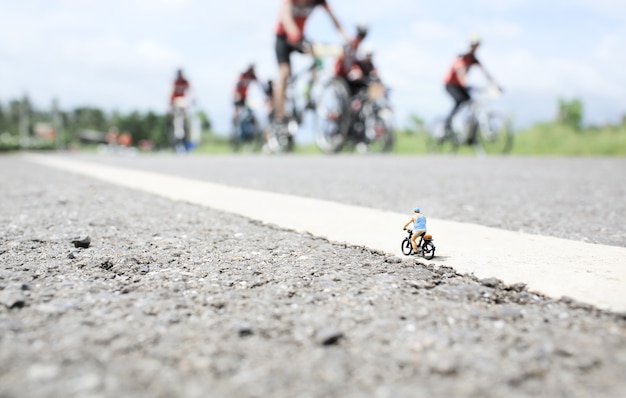 Stary człowiek miniaturowy na przejażdżkę rowerem w wiejskiej drodze z grupą tła wyścigu rowerowego.