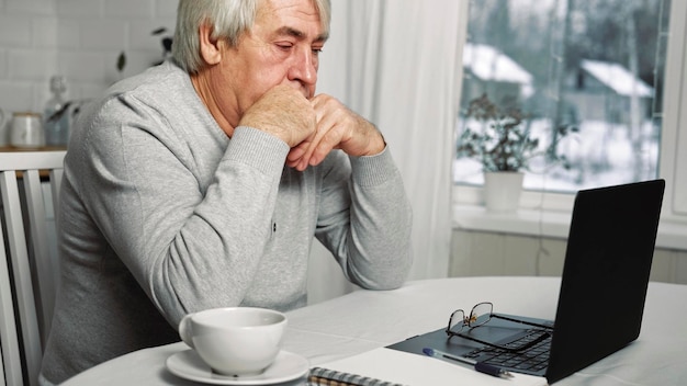 Stary człowiek myśli przy laptopie Zamyślony dojrzały Siwe włosy 60s 70s Starszy mężczyzna siedzi przy stole z laptopem Zamyślony emeryt Starszy mężczyzna pracuje online na komputerze z domu Rozwiązywanie problemów z rozwiązaniami