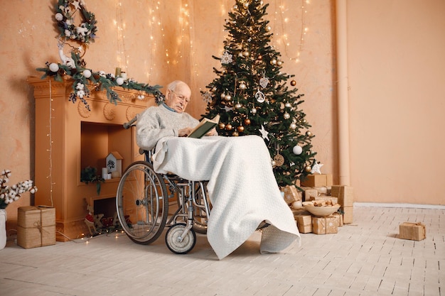 Stary człowiek na wózku inwalidzkim siedzący obok choinki i czytający książkę