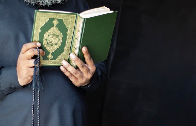 Zdjęcie stary człowiek trzymający i czytający obraz islamski z koranu na czarnym tle