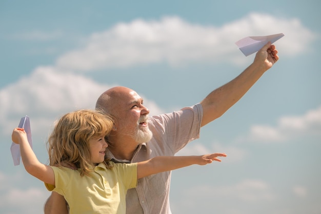 Stary dziadek i wnuk małego dziecka z papierowym samolotem nad błękitnym niebem i chmurami pokolenie mężczyzn gr