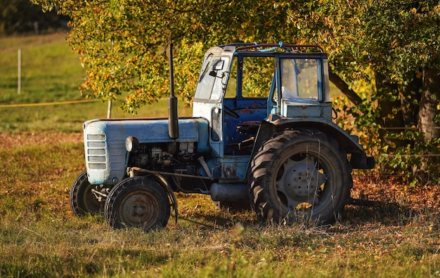 Stary niebieski, częściowo zardzewiały, traktor zaparkowany na jesiennej łące niewyraźne tło drzew