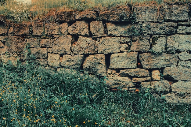Stary opuszczony kamienny mur wykonany ze starych kamieni porośniętych trawą i mchem
