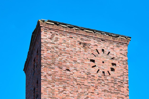 Stary opuszczony wieża z czerwonej cegły z okrągłym zegarem na elewacji na tle błękitnego nieba, fragment. Budynek przemysłowy murowany z cegły w stylu vintage, tło starożytnej architektury