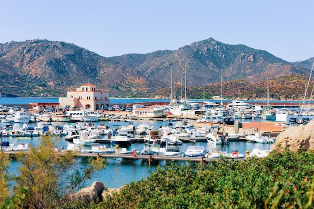 Zdjęcie stary port sardynii i marina ze statkami w pobliżu morza śródziemnego w mieście villasimius na wyspie południowej sardynii we włoszech w lecie. pejzaż miejski z jachtami i łodziami