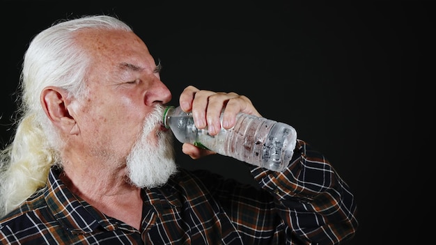 Stary siwowłosy mężczyzna pije wodę z plastikowej butelki Zdjęcie