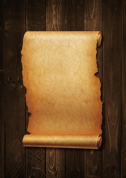 Stary średniowieczny arkusz papieru Zwój pergaminu na białym tle na tle deski drewnianej