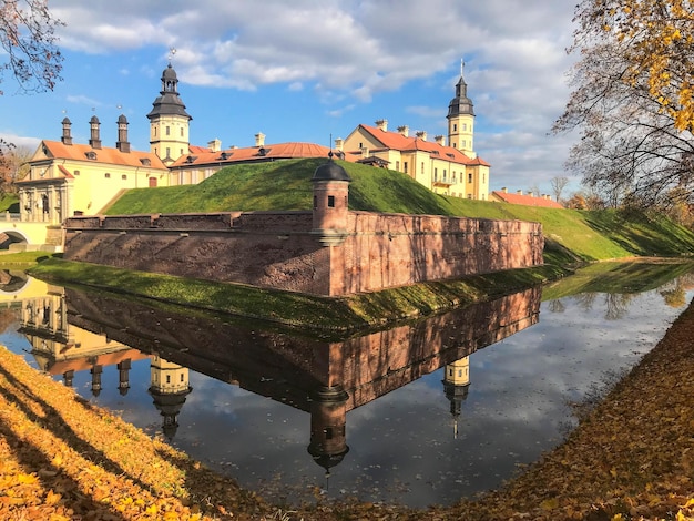 Stary starożytny średniowieczny zamek z iglicami i wieżami mury z kamienia i cegły otoczone fosą ochronną z wodą w centrum Europy Architektura w stylu barokowym