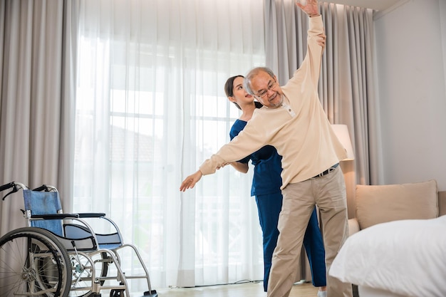 Stary starszy mężczyzna lubi trenować z fizjoterapeutą w zakresie wyciągniętych ramion w domu, azjatycki fizjoterapeuta pielęgniarski pomaga starszym ćwiczącym rozciąganie ramion, koncepcja rehabilitacji osób niepełnosprawnych