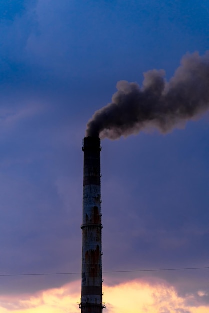 Stary wieku wyblakły wysoki przemysłowy komin fabryczny z dymem nad nim Pochmurne niebo w tle
