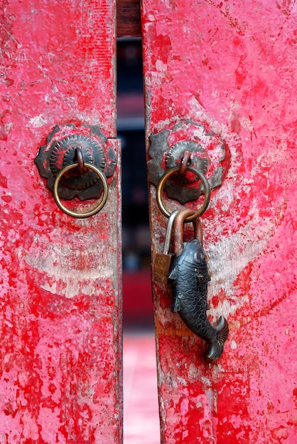Zdjęcie stary wyblakły czerwony malowane drewniane drzwi chiński tradycyjny styl z metalową rączką i zardzewiałym metalowym kółkiem w kształcie ryb.