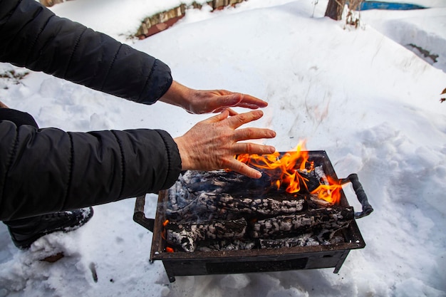 Starzec, którego ręka jest zimna w zimnym, śnieżnym powietrzu, grzeje dłoń w ogniu drewna.