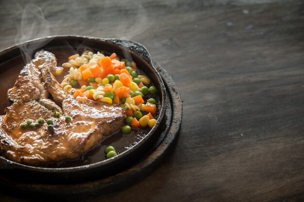 Zdjęcie stek wieprzowy podawany na gorącej patelni z sosem mus z marchewką i kukurydzą z góry na drewnianym stole